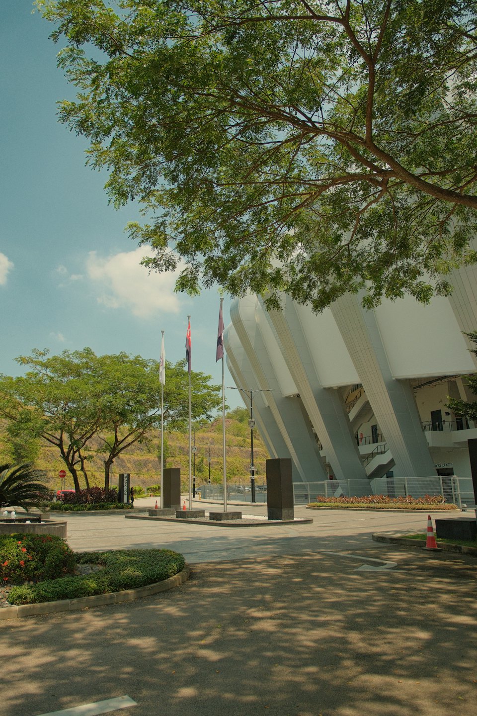 Modern white and grey building with trees and flagpoles.